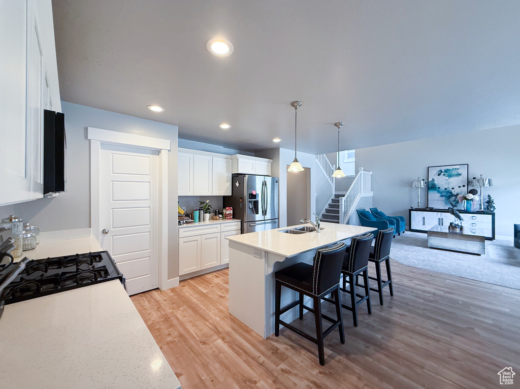 Kitchen featuring stainless steel refrigerator with ice dispenser, light wood-style floors, a kitchen breakfast bar, light countertops, and recessed lighting