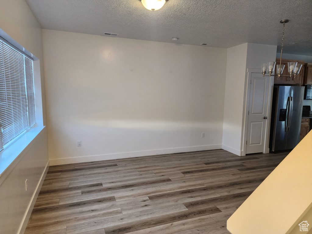 Unfurnished dining area featuring a chandelier, wood finished floors, a textured ceiling, and baseboards