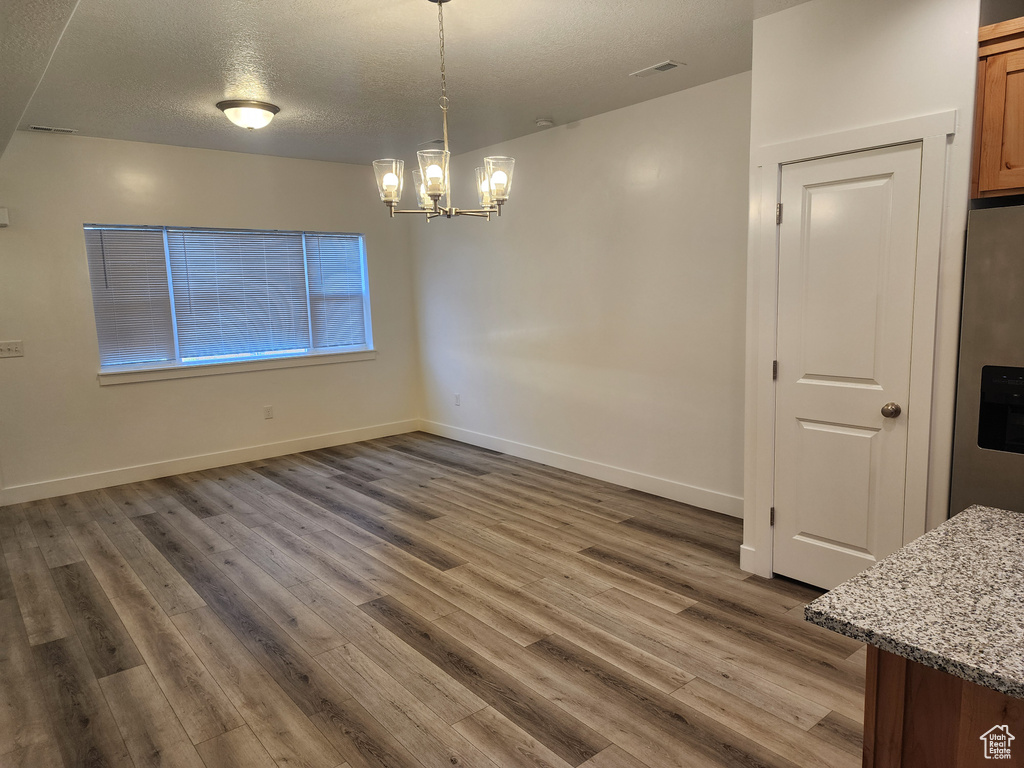 Unfurnished dining area featuring wood finished floors, a chandelier, a textured ceiling, and baseboards