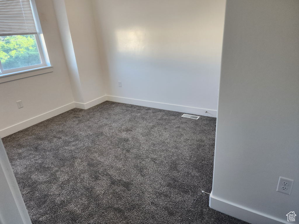 Spare room featuring dark carpet and baseboards