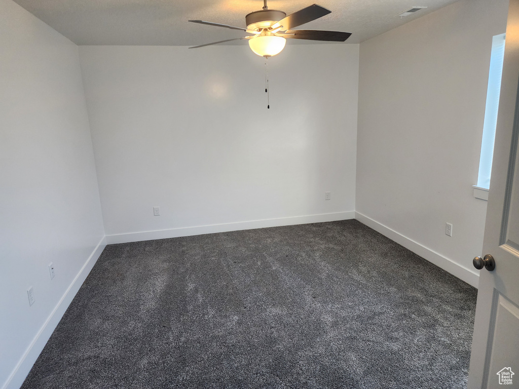 Spare room with a ceiling fan, dark colored carpet, and baseboards
