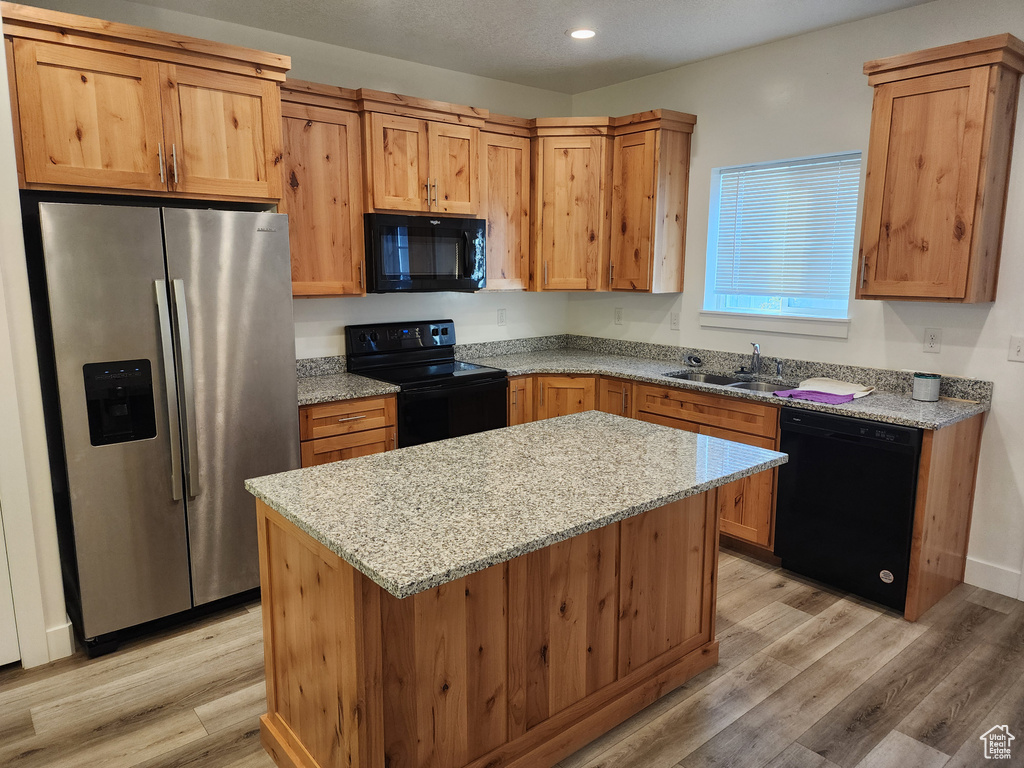 Kitchen featuring black appliances, a sink, light wood finished floors, light stone counters, and a center island