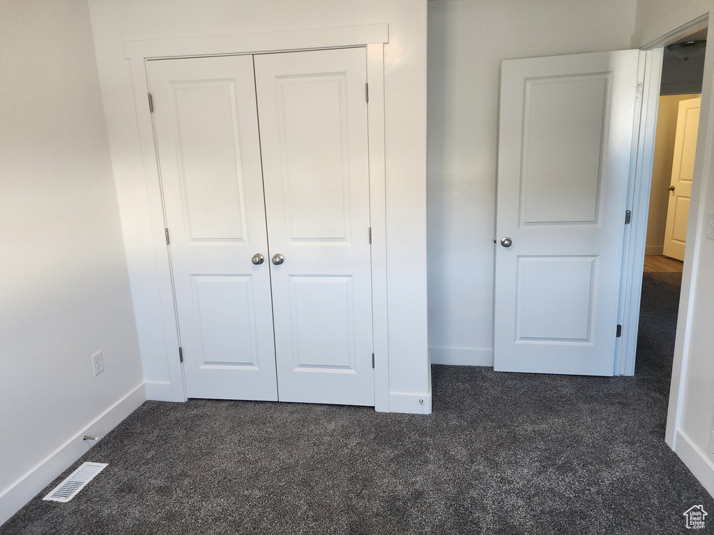 Unfurnished bedroom with dark carpet, baseboards, and a closet