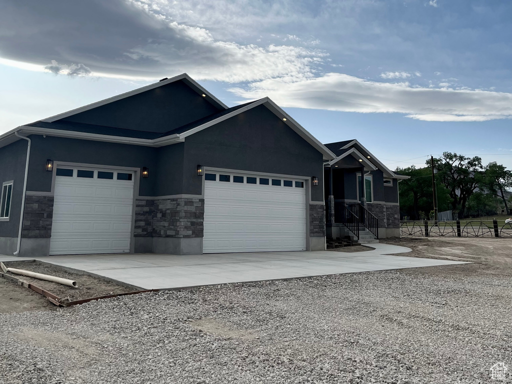 Ranch-style house with stone siding, a garage, concrete driveway, and stucco siding