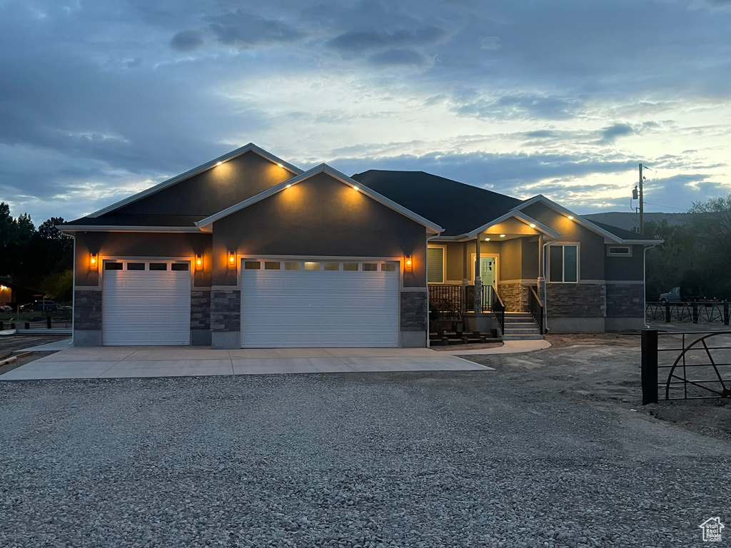 View of front of house featuring stone siding, gravel driveway, stucco siding, and a garage