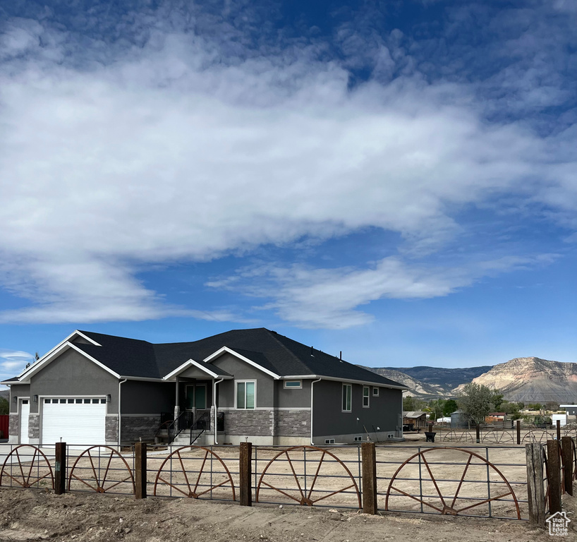 Ranch-style house featuring stone siding, a fenced front yard, a mountain view, a garage, and stucco siding