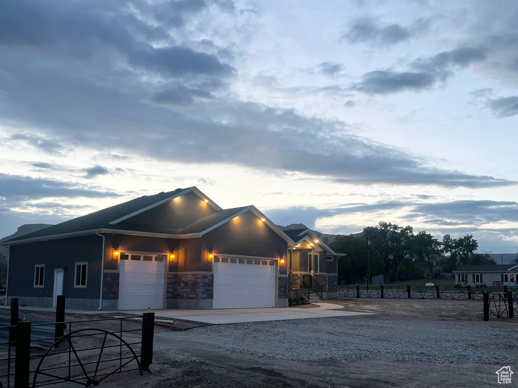 View of front of property with a garage, stone siding, driveway, and fence