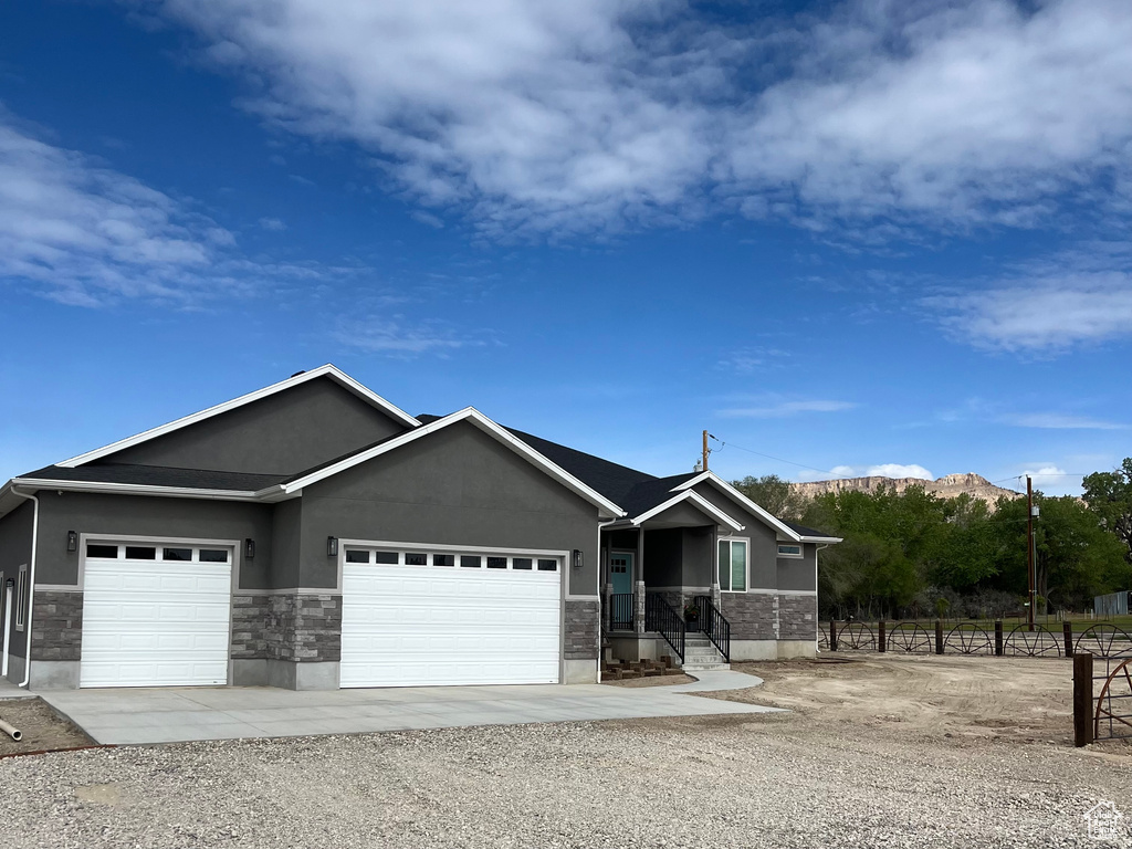 Ranch-style house with a garage, stucco siding, stone siding, driveway, and a mountain view