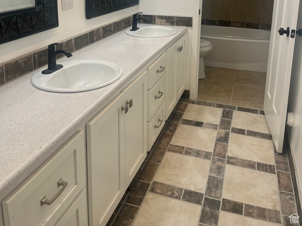 Bathroom with toilet, double vanity, stone finish floors, and a bathtub