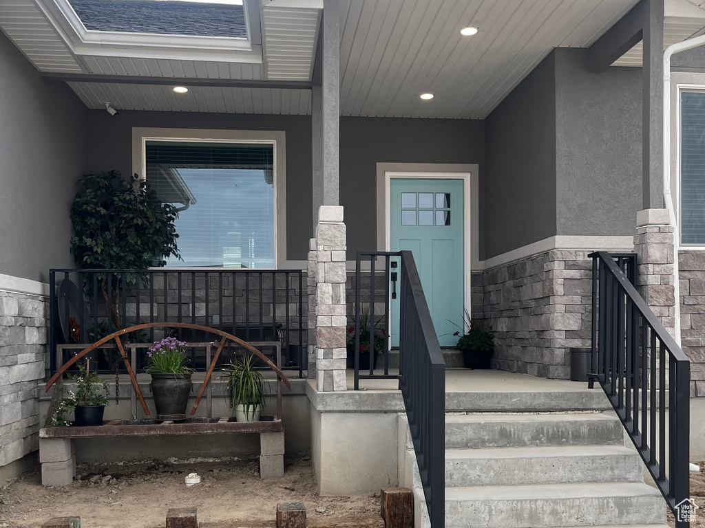 View of exterior entry featuring stucco siding, a porch, and stone siding