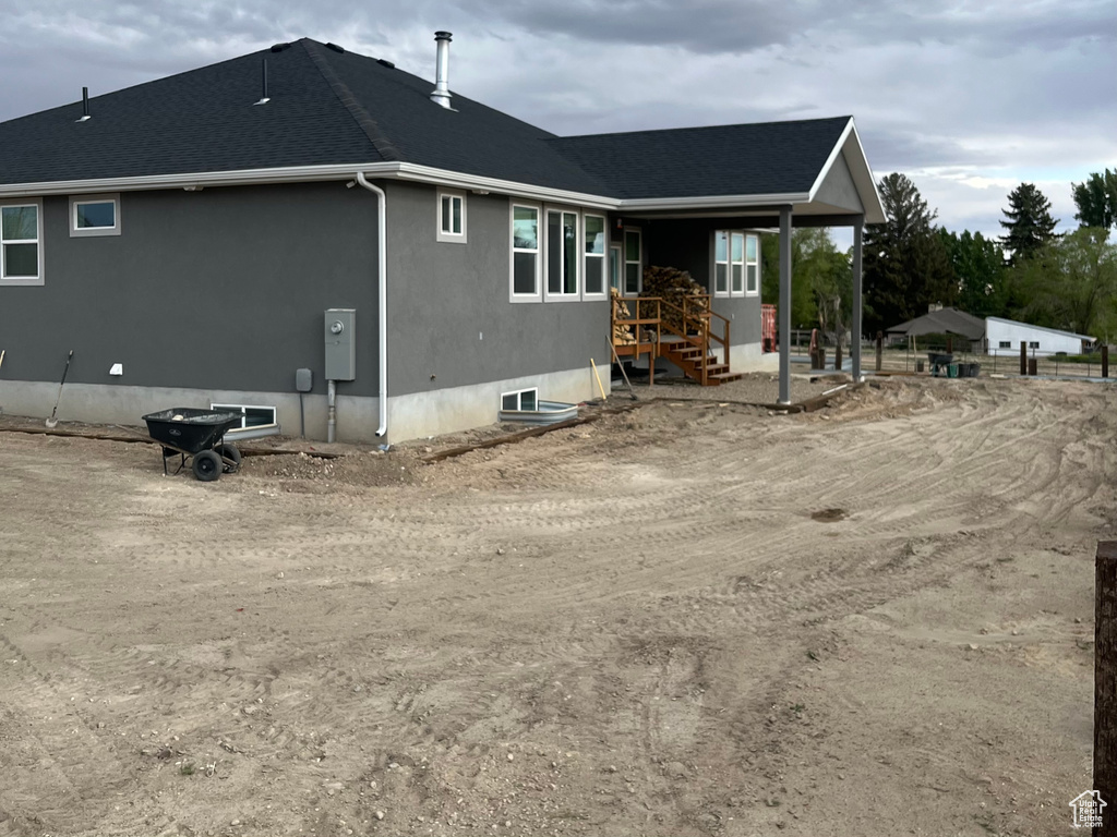 Back of property featuring a shingled roof and stucco siding