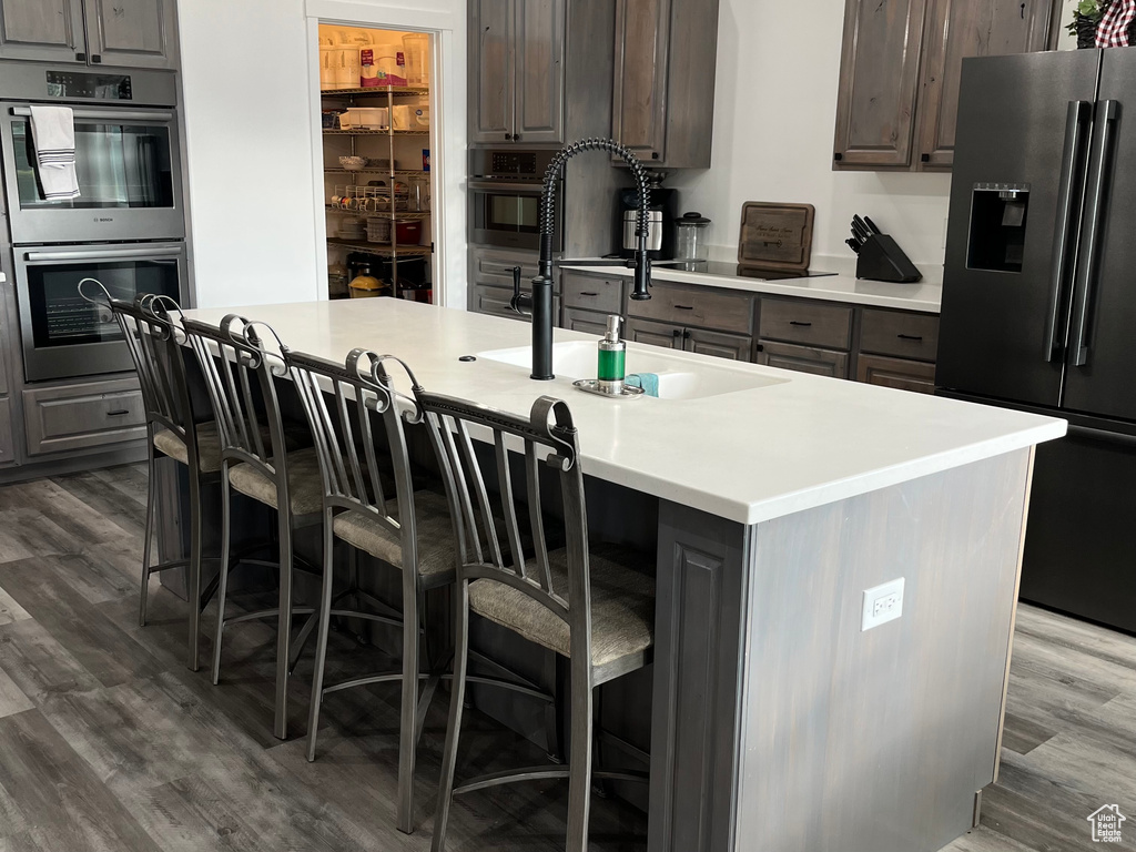 Kitchen featuring high end refrigerator, stainless steel double oven, dark wood finished floors, light countertops, and a breakfast bar area