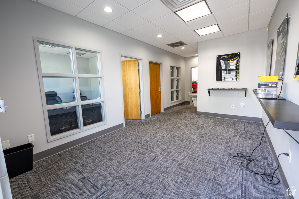 Unfurnished office with dark colored carpet, baseboards, and a drop ceiling