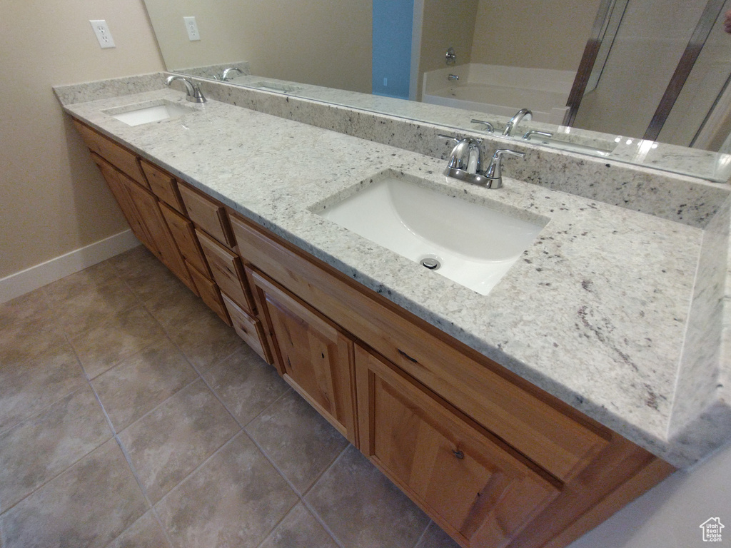 Full bathroom featuring double vanity, baseboards, tile patterned flooring, and a bath
