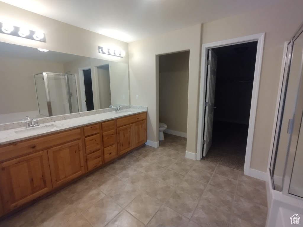 Bathroom featuring a shower stall, toilet, double vanity, and tile patterned floors