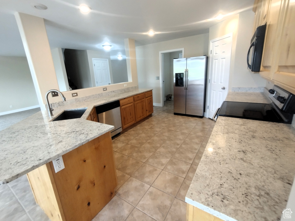 Kitchen with appliances with stainless steel finishes, a sink, baseboards, a peninsula, and light stone counters