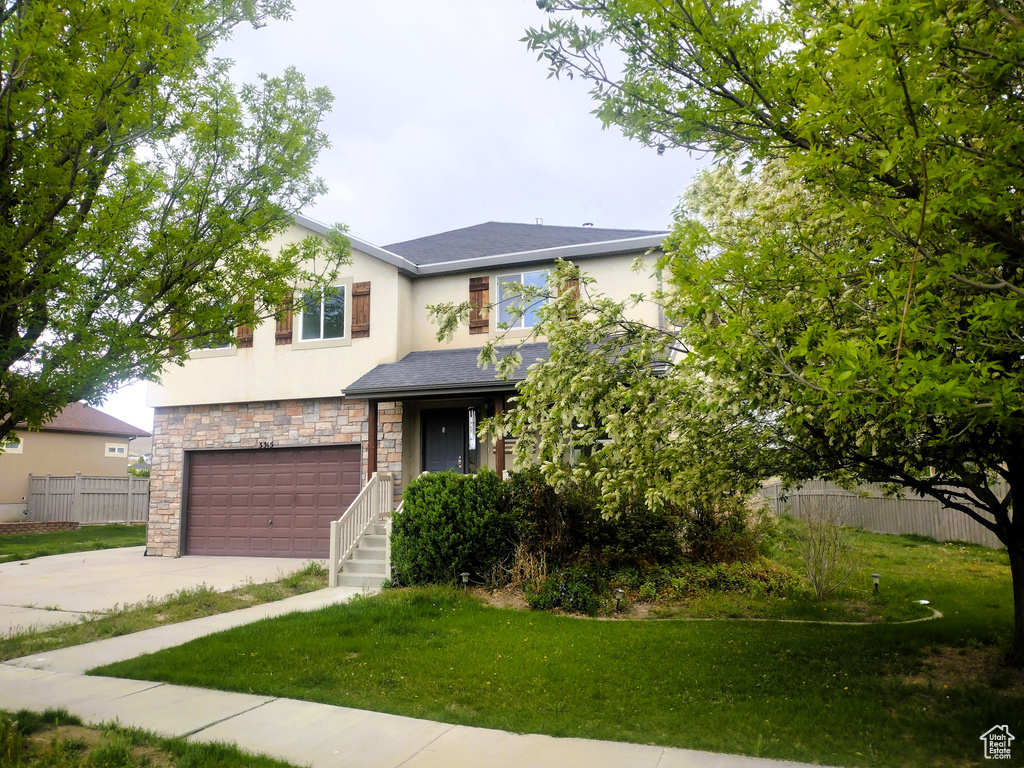 View of front of home with stucco siding, an attached garage, driveway, and stone siding
