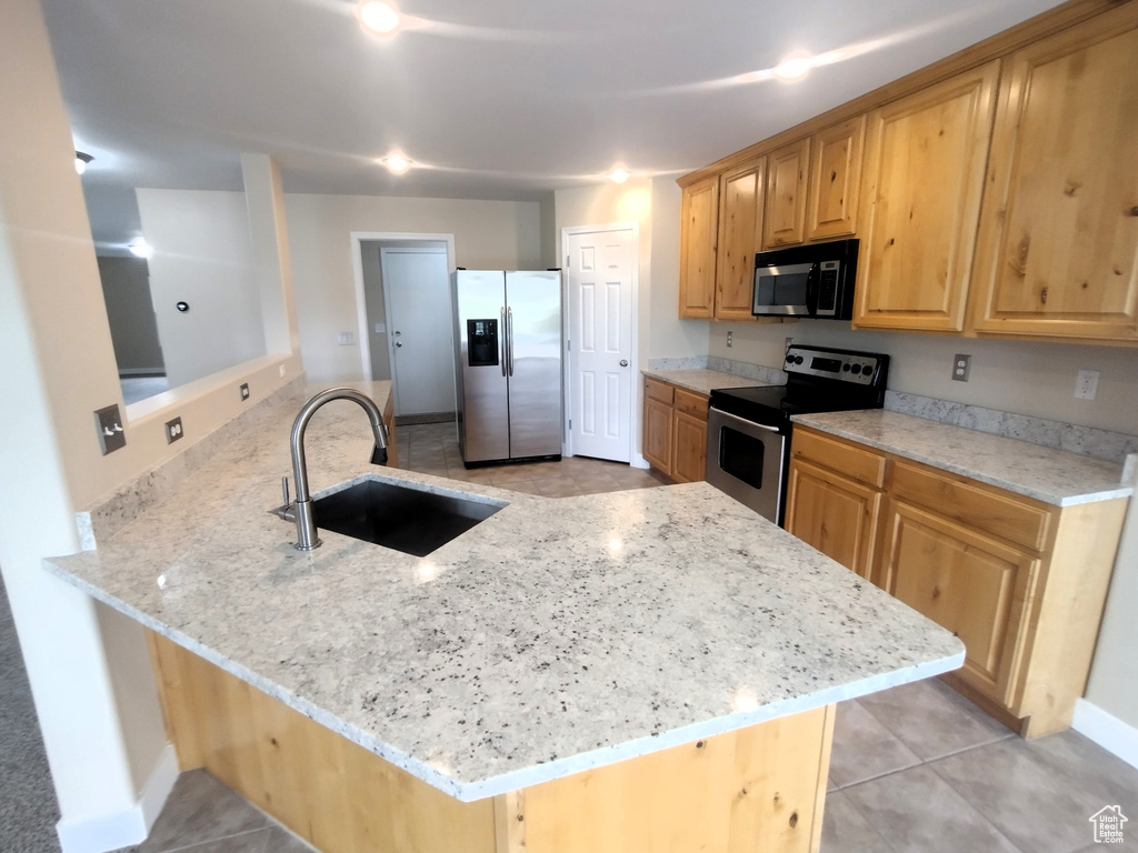 Kitchen with stainless steel appliances, a sink, a peninsula, light stone countertops, and light tile patterned flooring