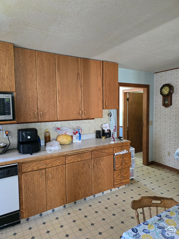 Kitchen featuring dishwasher, stainless steel microwave, light countertops, light floors, and a textured ceiling