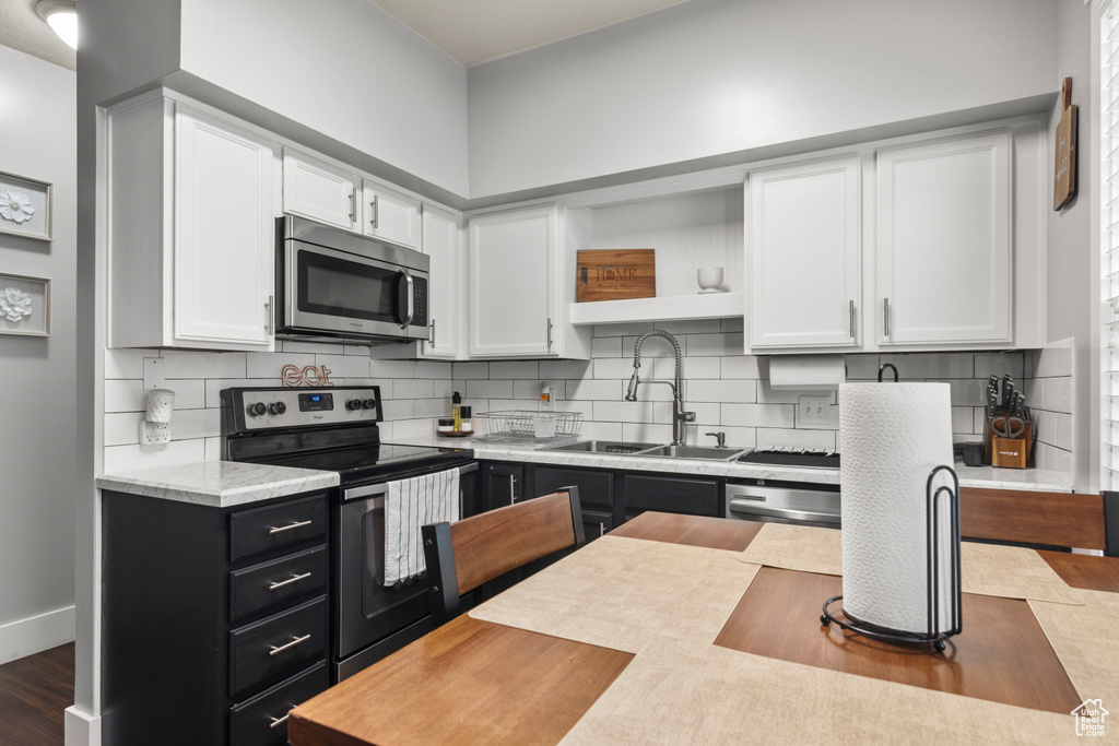 Kitchen with stainless steel appliances, white cabinets, light countertops, a sink, and dark cabinetry