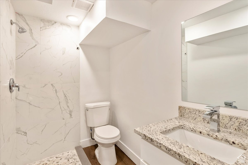 Bathroom with toilet, a marble finish shower, wood finished floors, vanity, and baseboards