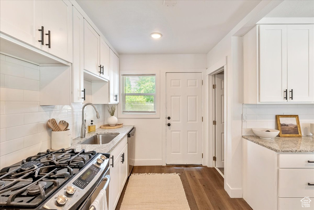 Kitchen featuring stainless steel appliances, a sink, dark wood-type flooring, white cabinetry, and light stone counters