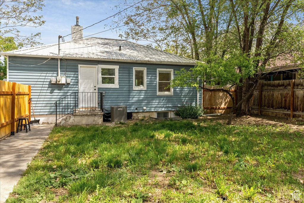 Back of house featuring a fenced backyard, metal roof, a chimney, and cooling unit