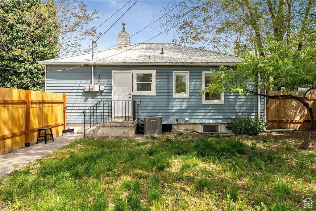 Back of property with fence, metal roof, a chimney, and central AC