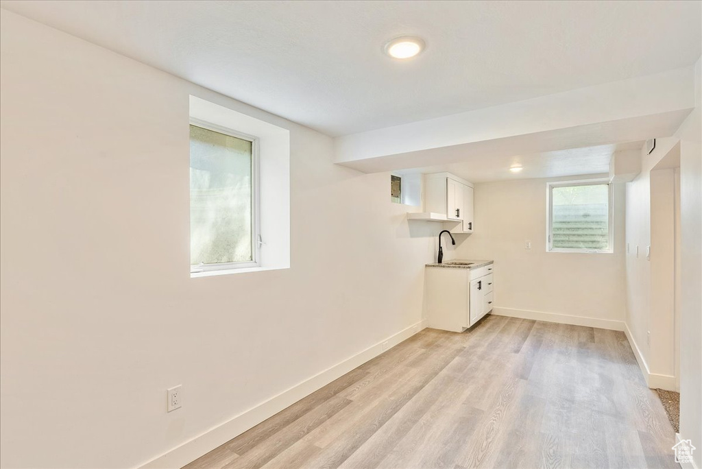 Basement with a sink, baseboards, light wood-style floors, and plenty of natural light
