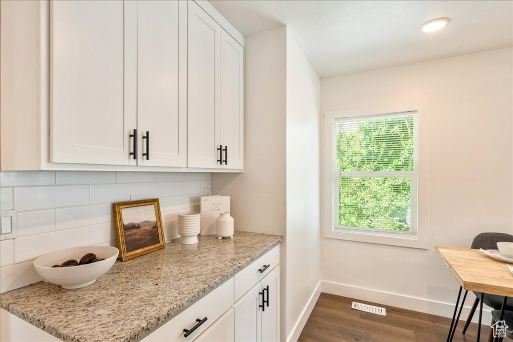 Kitchen with baseboards, dark wood-style floors, backsplash, white cabinets, and light stone countertops