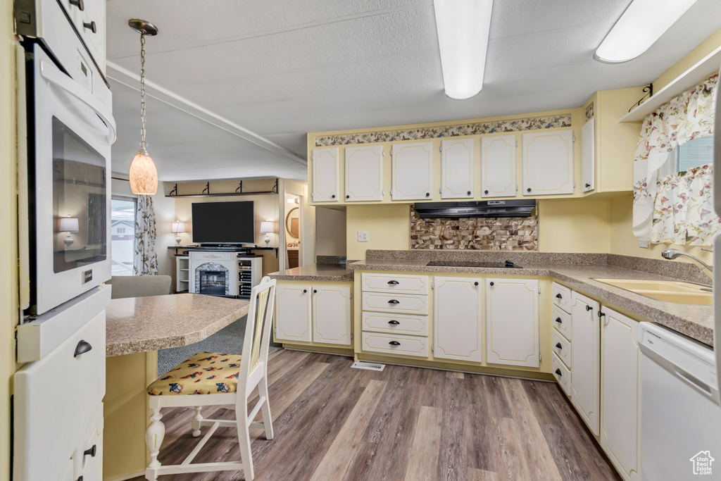 Kitchen with white appliances, under cabinet range hood, a sink, wood finished floors, and a fireplace
