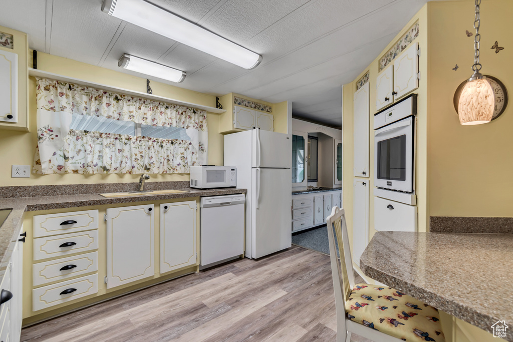 Kitchen featuring white appliances, a sink, light wood-type flooring, white cabinetry, and dark countertops