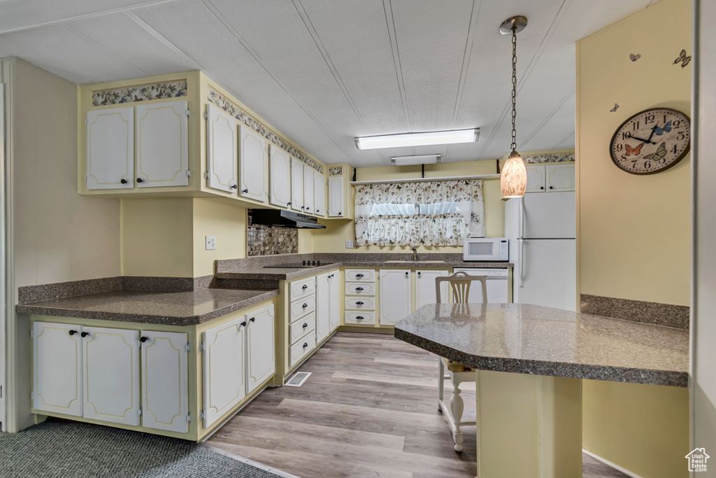 Kitchen featuring white appliances, under cabinet range hood, dark countertops, light wood-style flooring, and pendant lighting