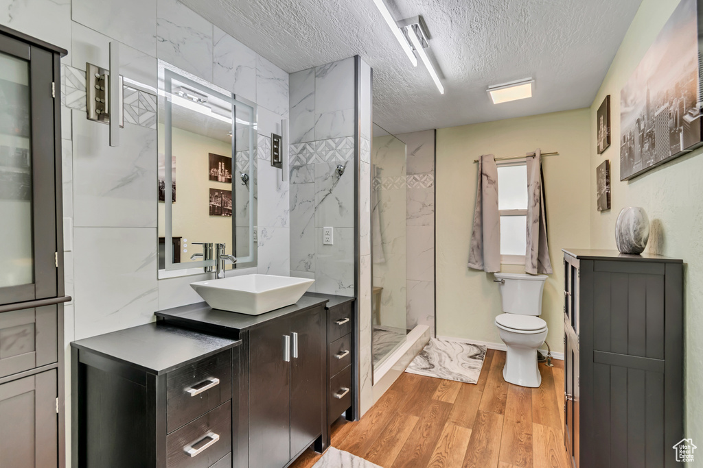Bathroom featuring a textured ceiling, wood finished floors, a marble finish shower, toilet, and vanity