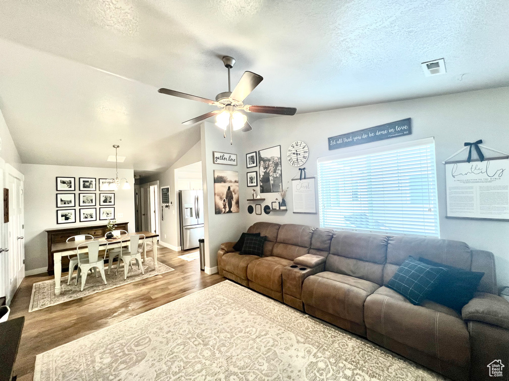 Living area featuring vaulted ceiling, wood finished floors, ceiling fan, a textured ceiling, and baseboards