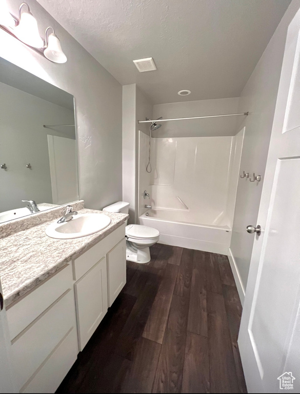 Bathroom featuring tub / shower combination, wood finished floors, toilet, vanity, and a textured ceiling