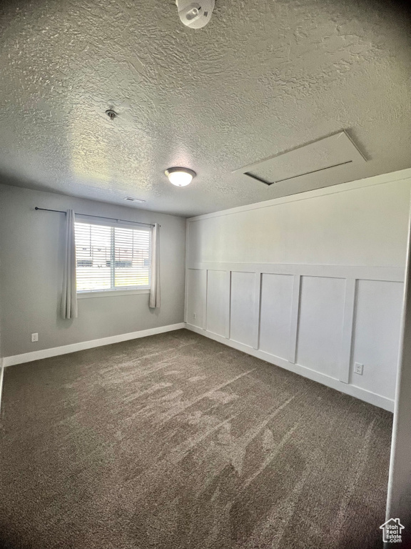 Unfurnished room with a textured ceiling, attic access, dark carpet, a decorative wall, and a wainscoted wall