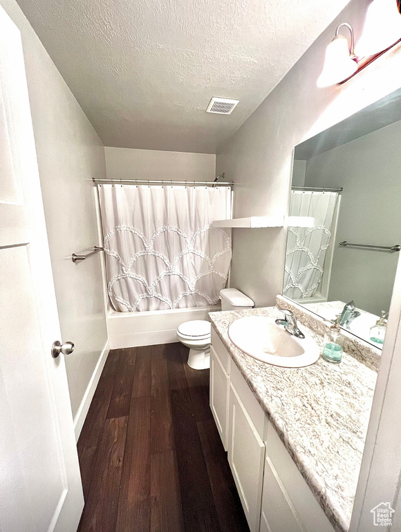 Full bath with wood finished floors, a textured ceiling, toilet, vanity, and baseboards