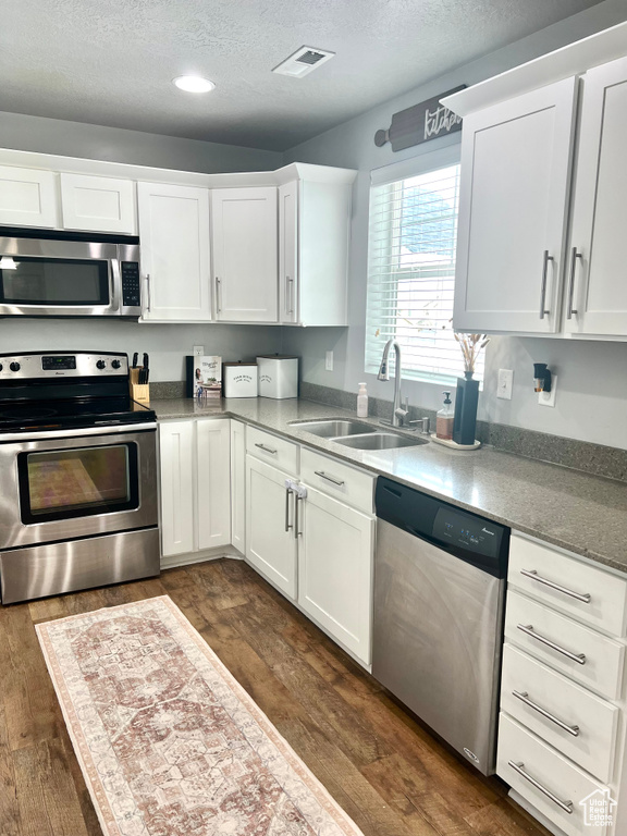 Kitchen with appliances with stainless steel finishes, dark wood-style floors, a textured ceiling, a sink, and white cabinetry