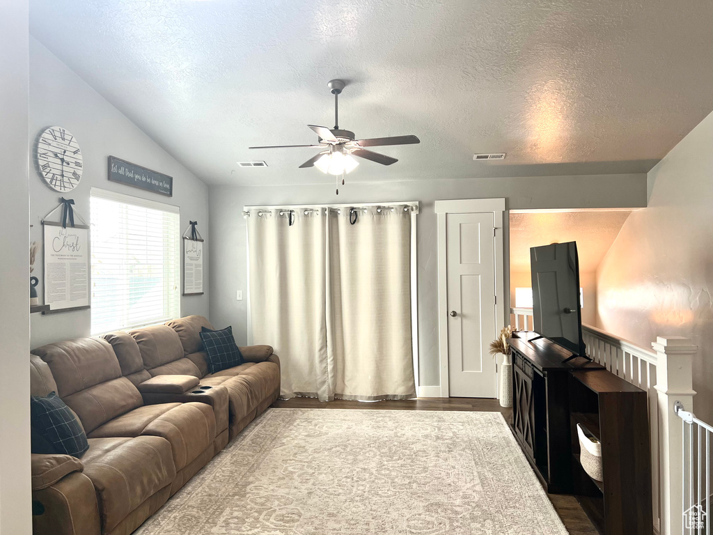Living area featuring a ceiling fan, vaulted ceiling, a textured ceiling, and wood finished floors