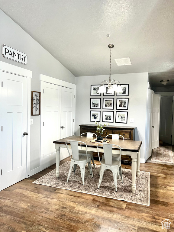 Dining area featuring a chandelier, wood finished floors, lofted ceiling, a textured ceiling, and baseboards