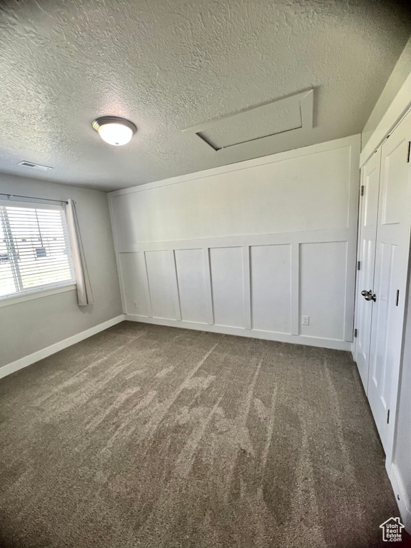 Carpeted empty room with attic access, a decorative wall, a textured ceiling, and a wainscoted wall