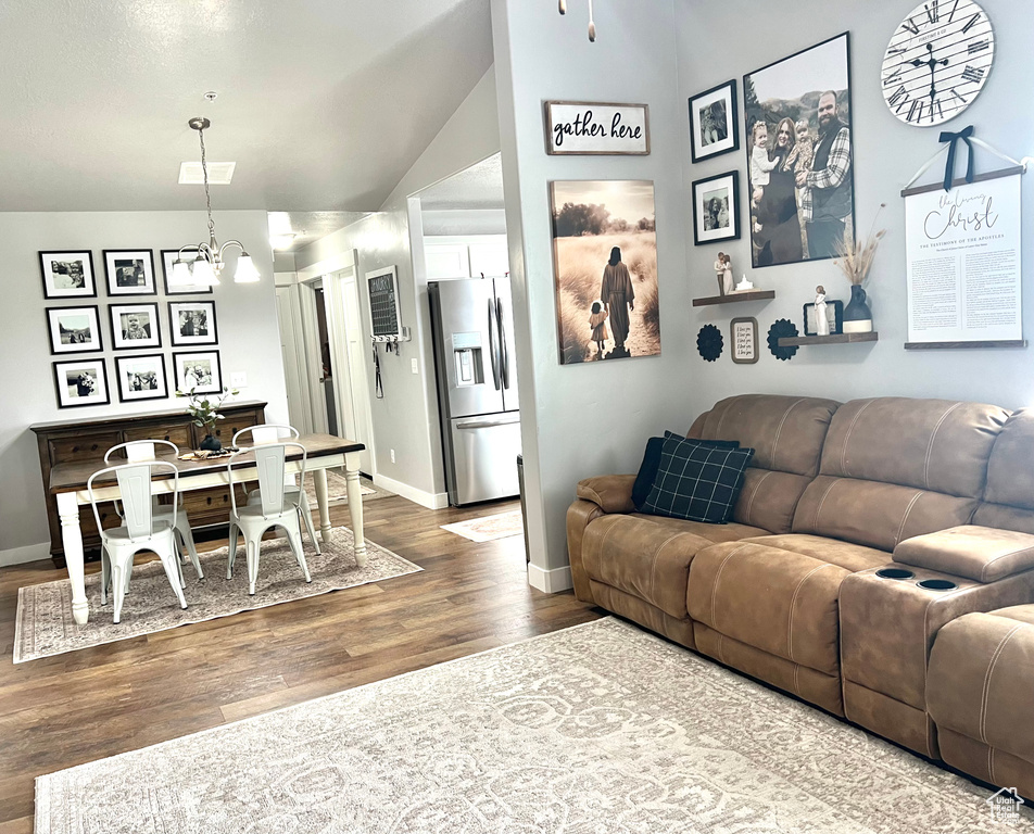 Living room featuring wood finished floors, a chandelier, baseboards, and lofted ceiling