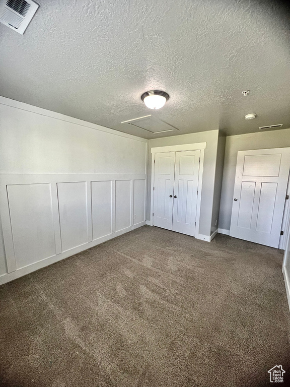 Unfurnished bedroom featuring a textured ceiling, carpet floors, attic access, and a closet