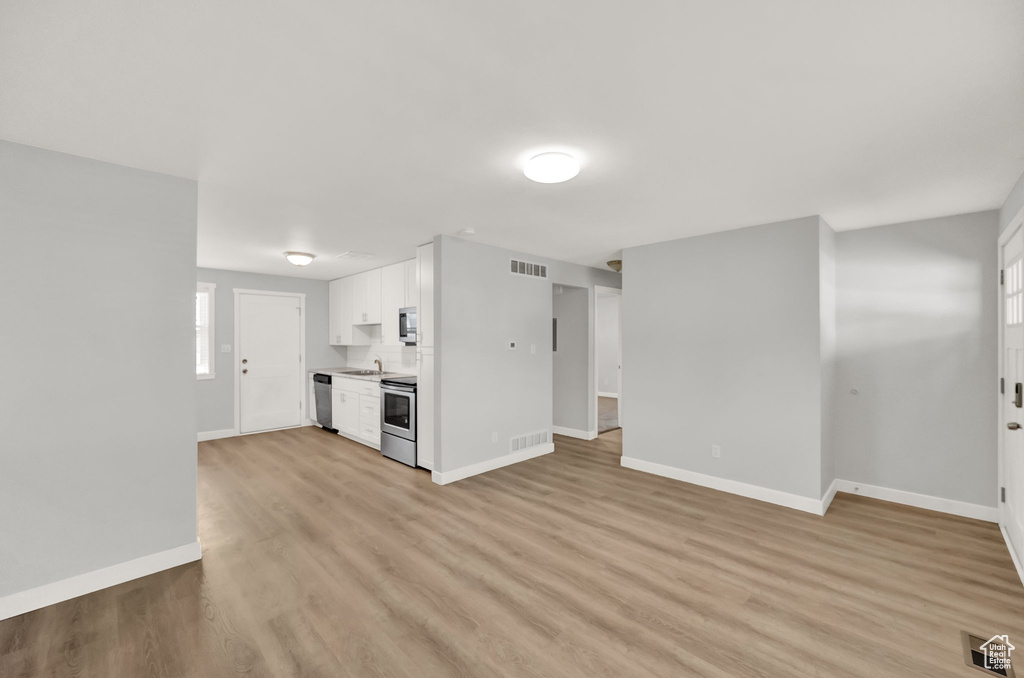 Unfurnished living room featuring a sink, baseboards, and light wood-style floors