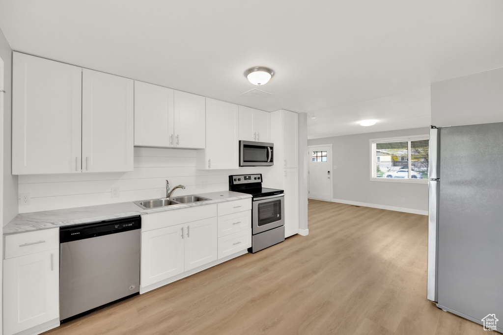 Kitchen with appliances with stainless steel finishes, a sink, light countertops, and white cabinetry