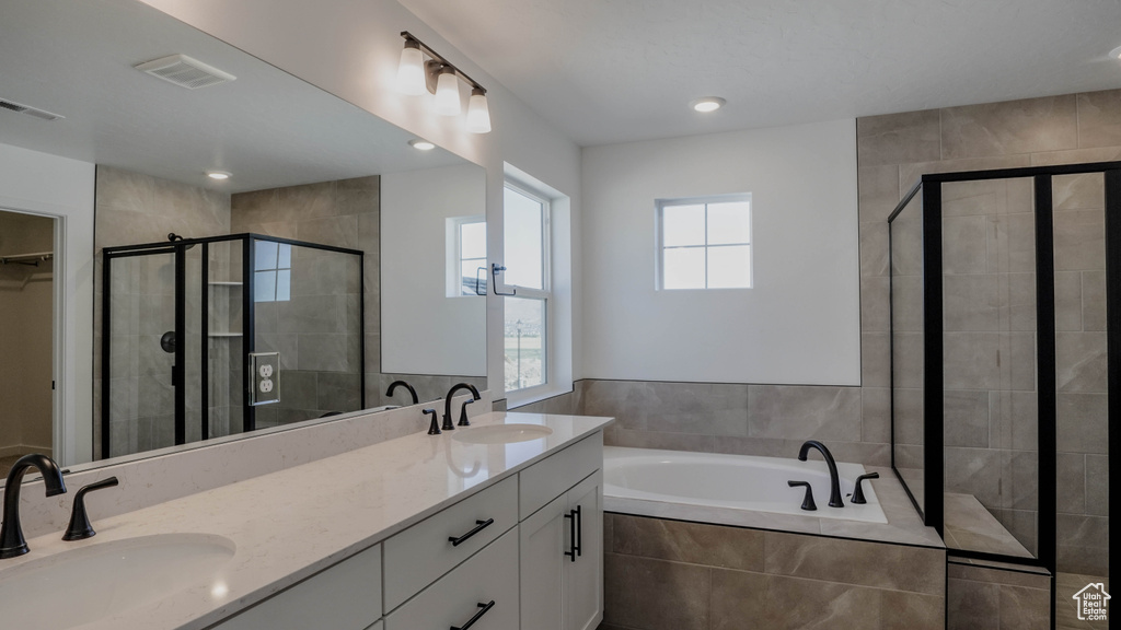 Bathroom featuring a bath, a stall shower, double vanity, a walk in closet, and recessed lighting