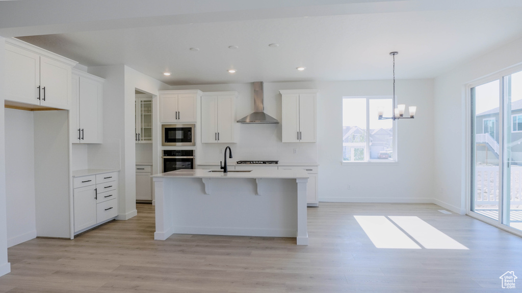 Kitchen featuring wall chimney range hood, black microwave, oven, light wood finished floors, and white cabinetry