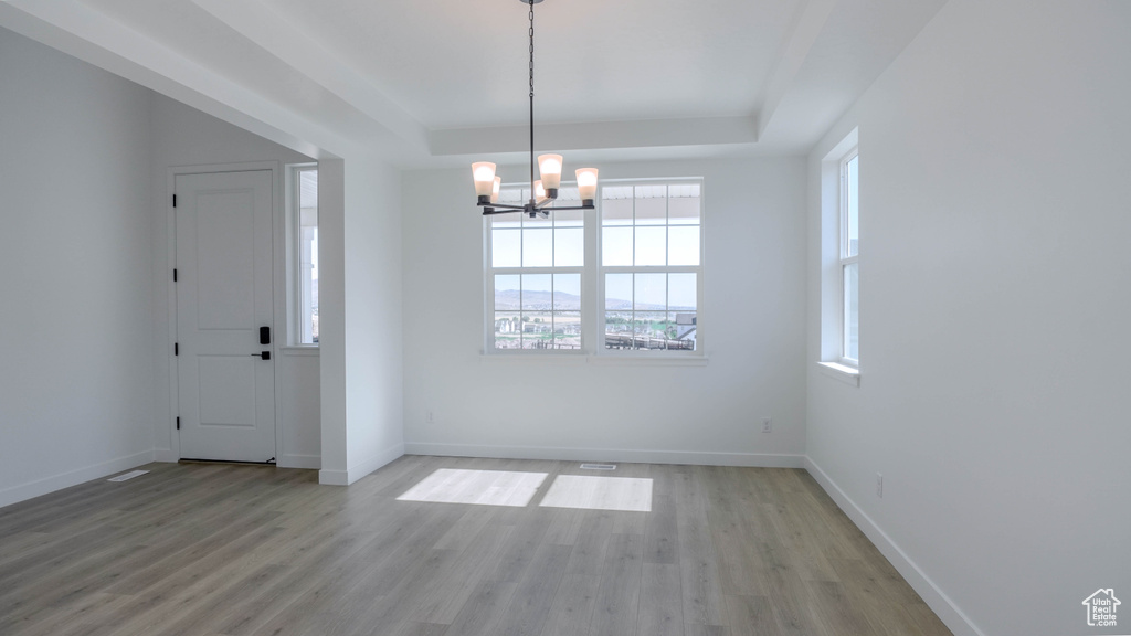 Empty room featuring a chandelier, light wood-type flooring, and a tray ceiling