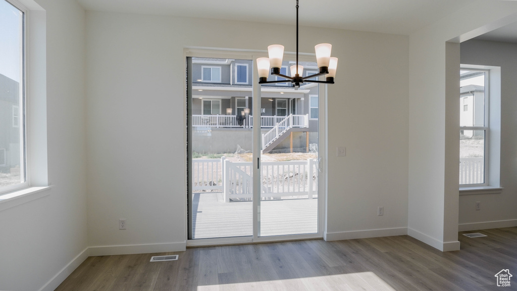 Unfurnished dining area with wood finished floors, healthy amount of natural light, and a chandelier